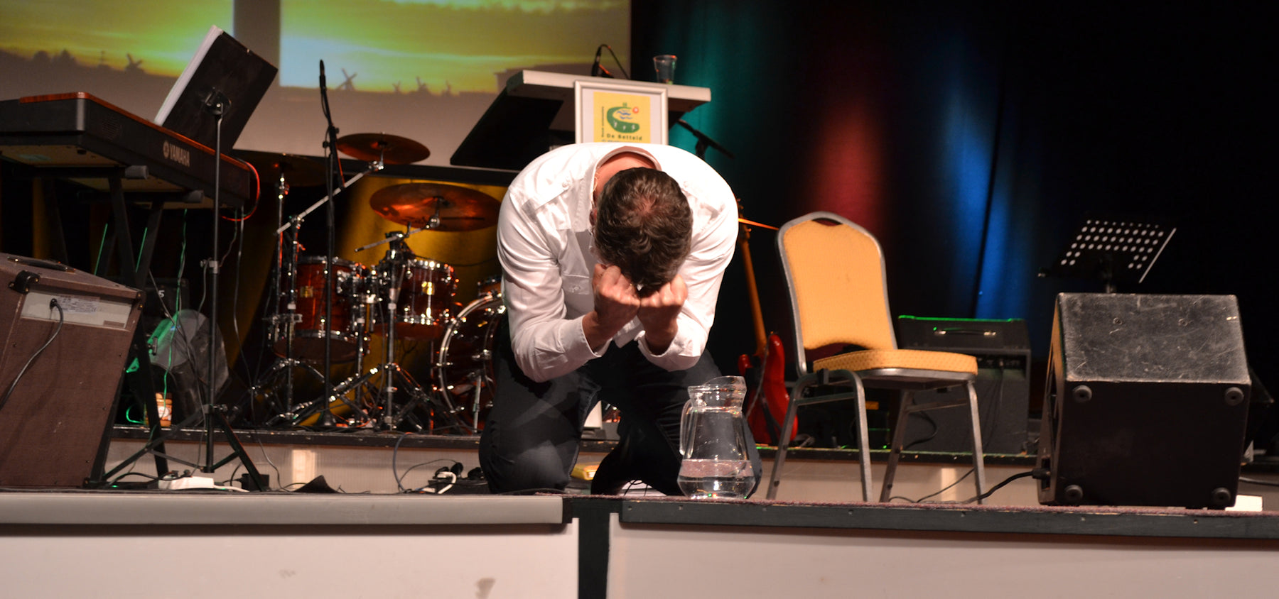 Spreker knielt in gebed op het podium van een Herstelconferentie